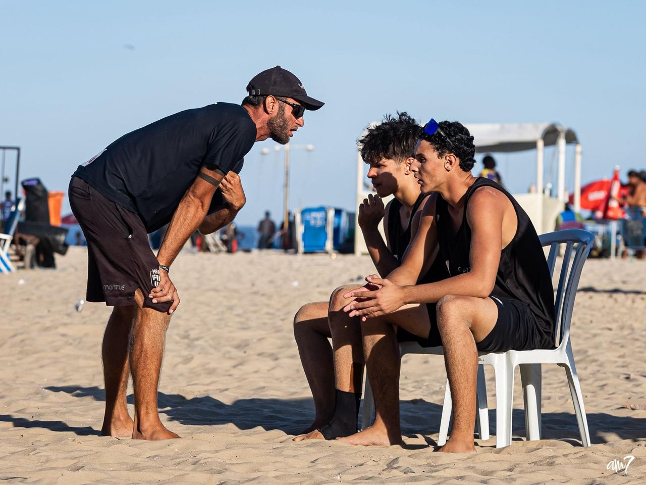 Treinador orientando dois atletas jovens na areia